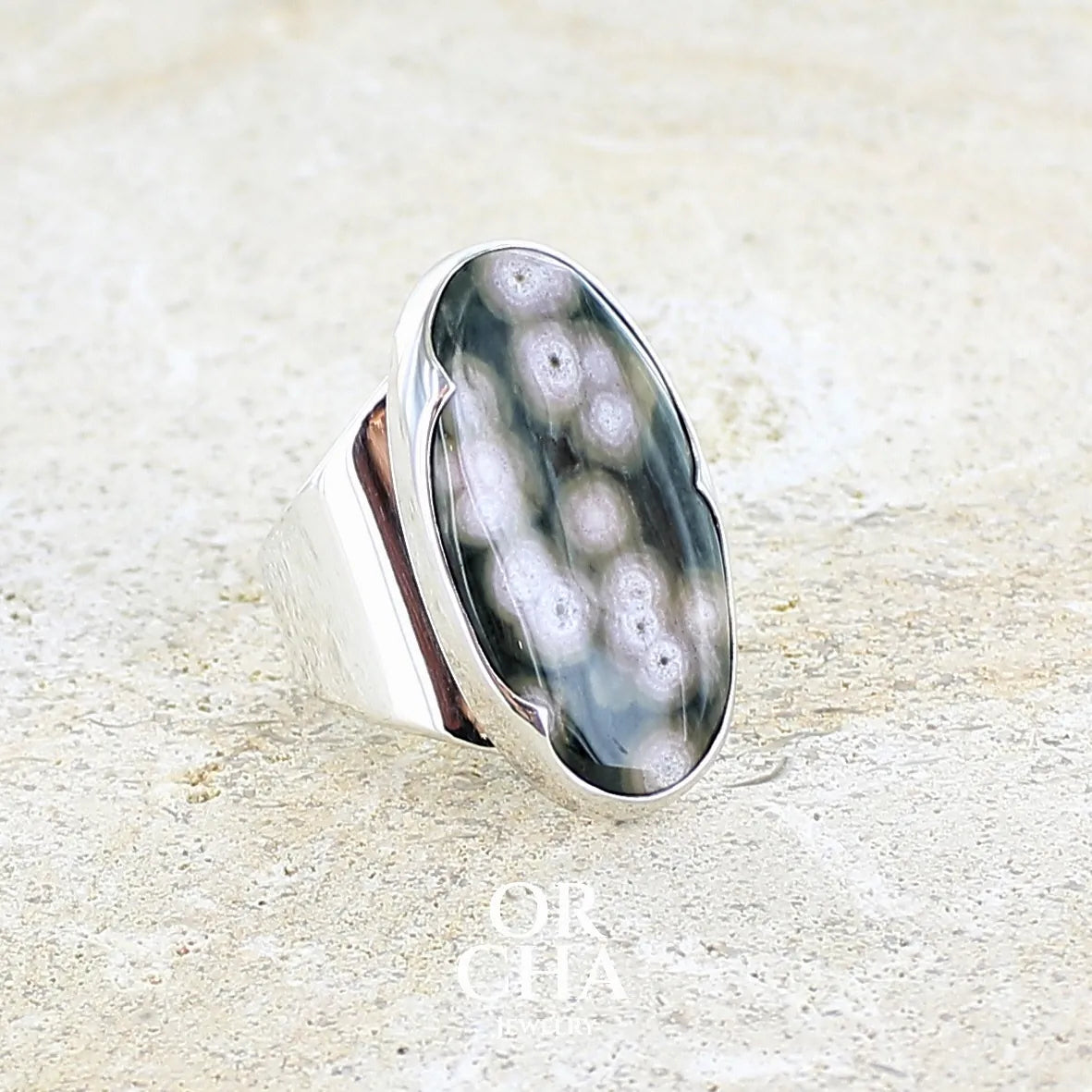 sertissage d'une bague pour femme en argent massif sertie d'un cabochon ovale de jaspe orbiculaire de couleur vert kaki, blanc et rosé. Pierre de qualité opaque. Bijou unique réalisée en taille 58 par Orchajewelry