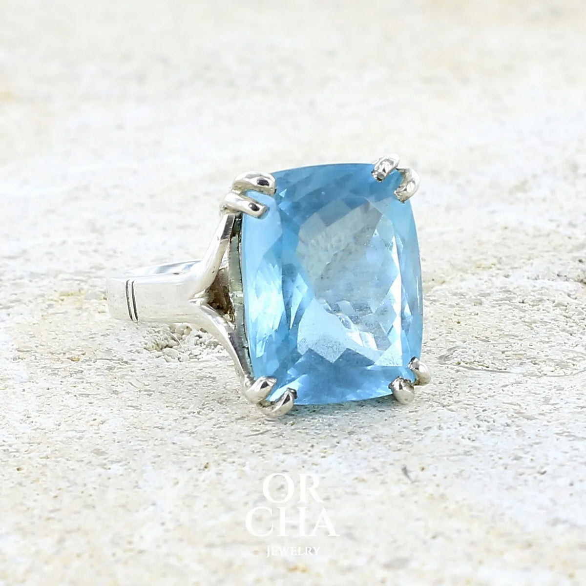 détail du sertissage d'une bague pour femme en argent massif sertie d'une magnifique aigue marine taillée de 10,3 carats de couleur bleue clair intense. Pierre transparente lumineuse comportant de légères inclusions. Bijou unique réalisée en taille 54 par Orchajewelry
