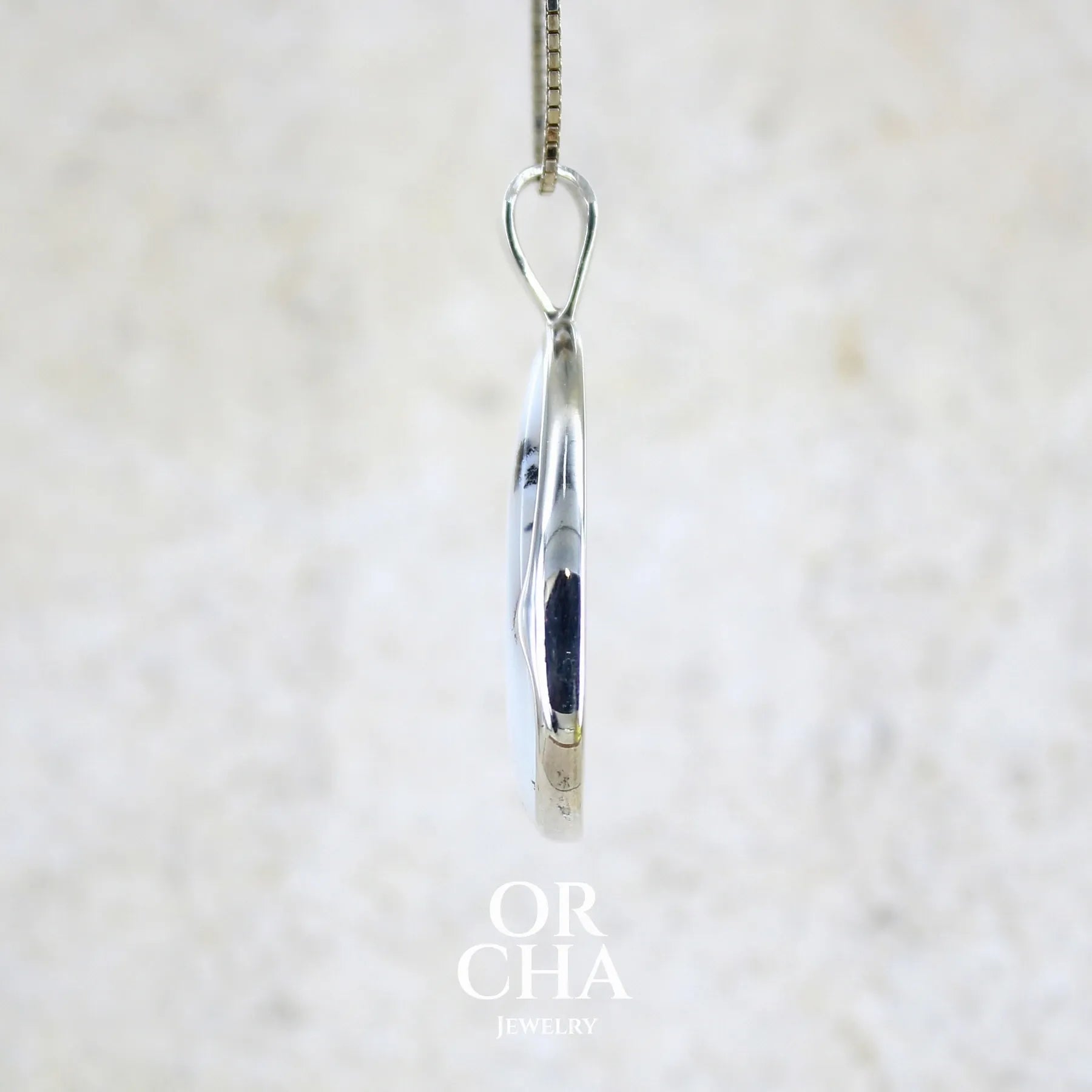 Détail du sertissage d'un pendentif pour femme en argent massif sertie d'un cabochon en forme de goutte  d'agate dendritique de couleur blanc pur et noir. Pierre opaque à translucide à inclusions paysages de dendrites de manganèse noires contrastées. Bijou unique réalisé par Orchajewelry