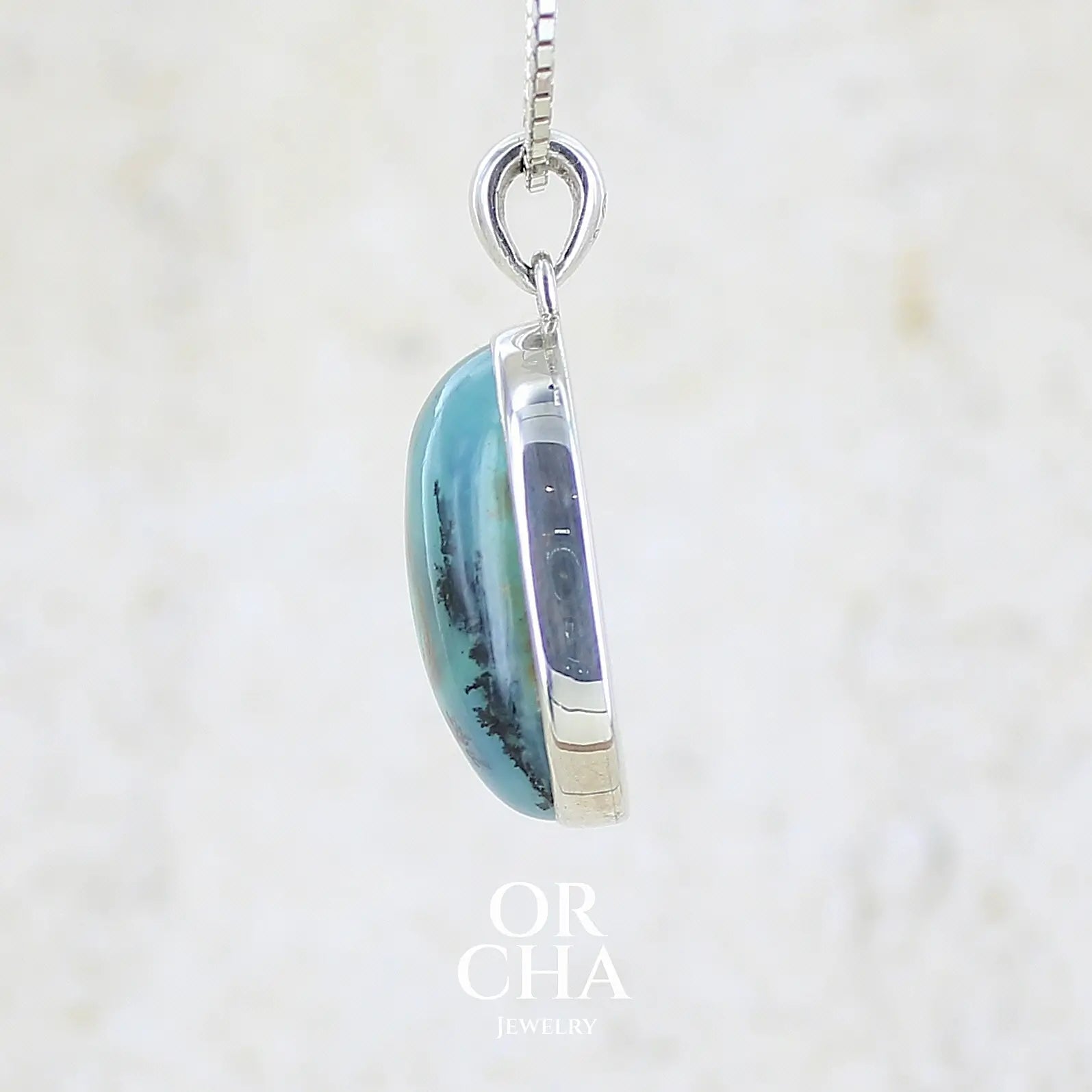 détail du sertissage d'un pendentif en argent massif, sertie d'un cabochon ovale d'opale bleue du Pérou de couleur bleu laiteux foncé à inclusions de dendrites paysages noires et de roche mère marron. Pierre opaque et translucide. Bijoux unique, éthique et durable présenté dans un coffret de notre marque, prêt à offrir. Livraison offerte, certificat d'authenticité, service client.