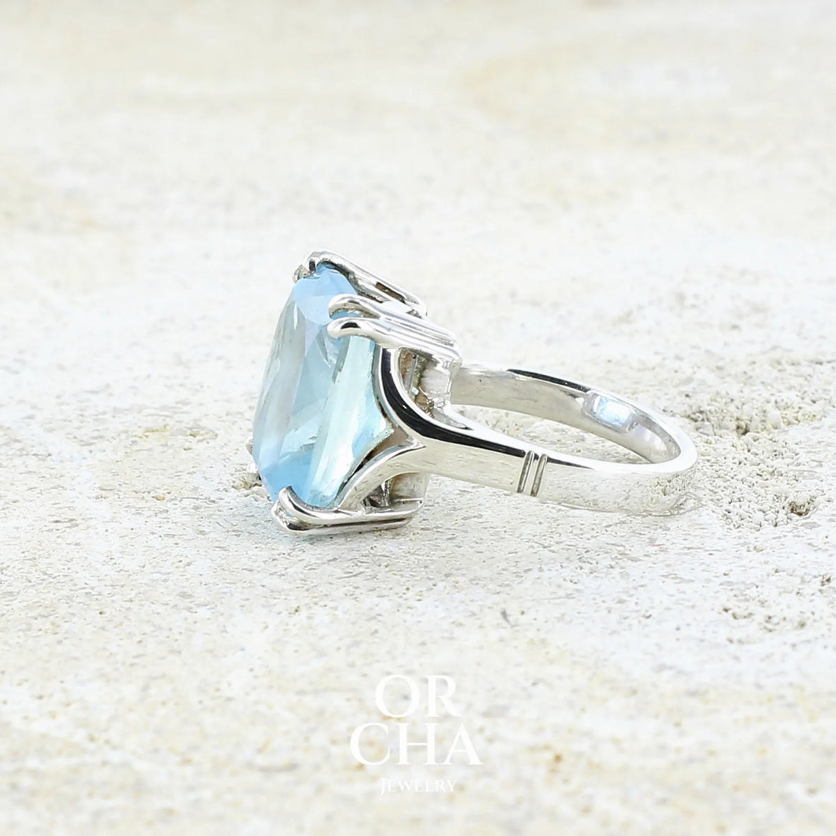 Vue détaillée d'une bague pour femme en argent massif sertie d'une magnifique aigue marine taillée de 10,3 carats de couleur bleue clair intense. Pierre transparente lumineuse comportant de légères inclusions. Bijou unique réalisée en taille 54 par Orchajewelry
